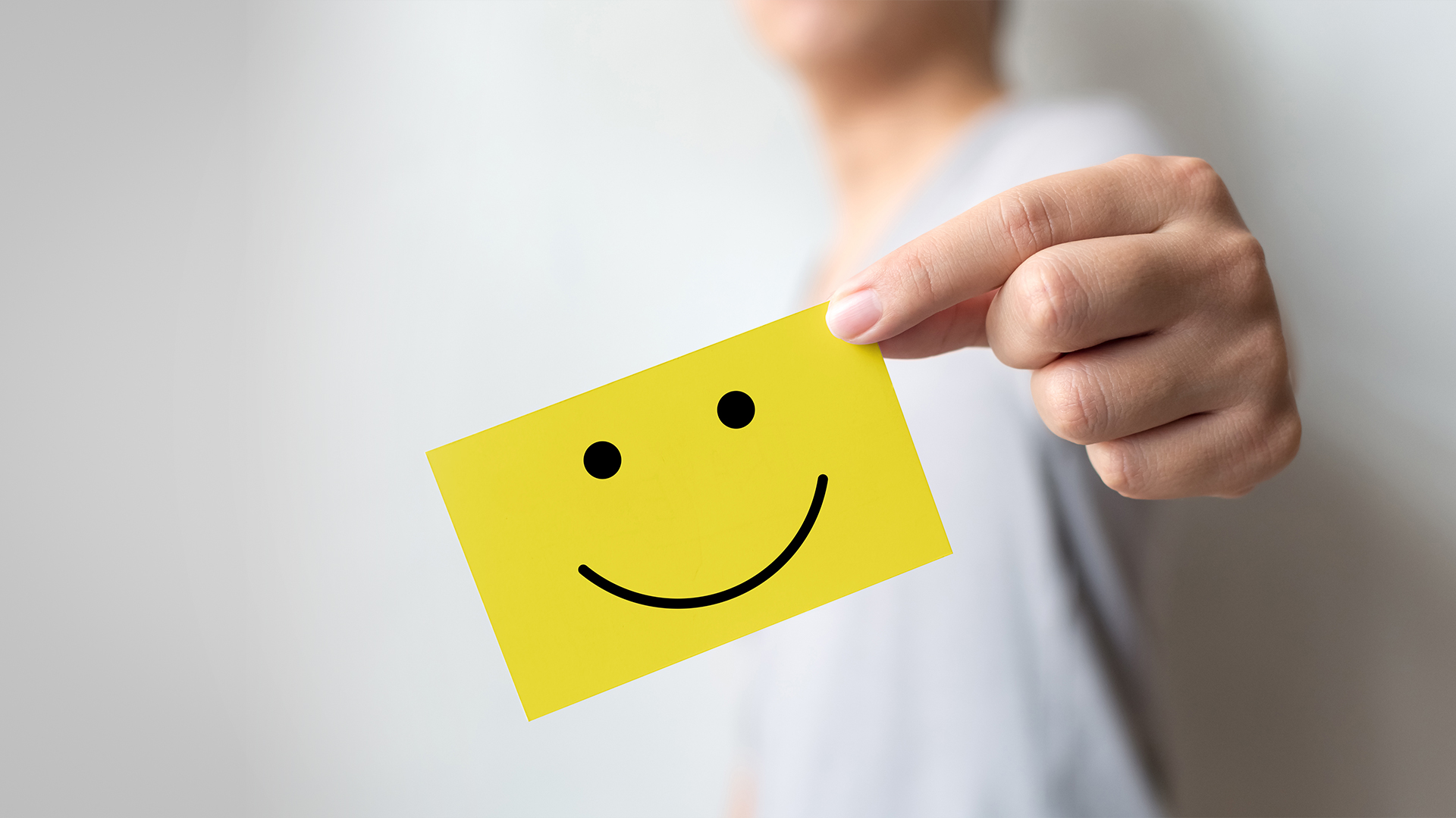 Person holding yellow card with smiley face, representing customer loyalty programs