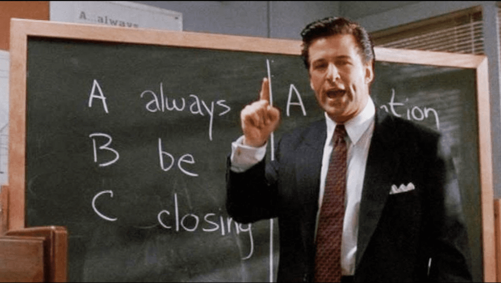 Man in suit standing in front of chalkboard talking about sales