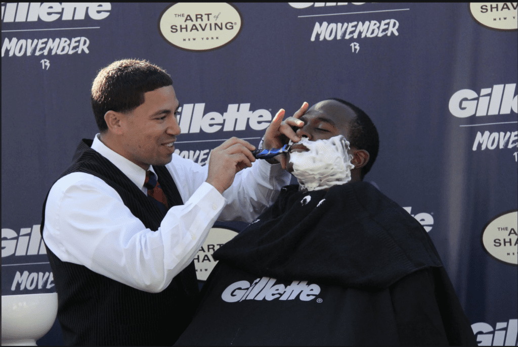 Man getting a shave from a barber during a Gillette Movember event, an example of a nonprofit-corporate partnership