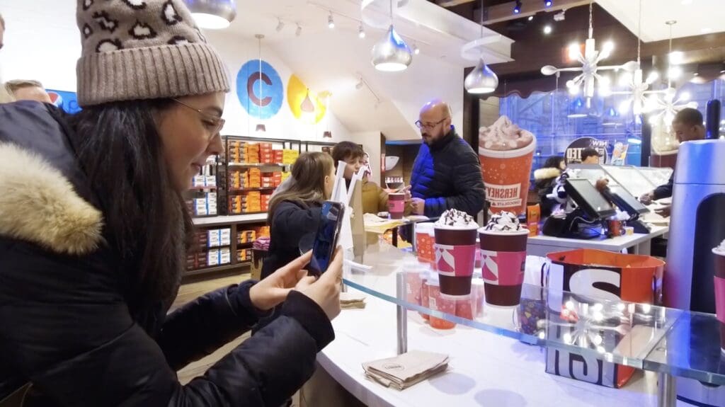 Hershey Case Study Image- a woman wearing a puffer jacket and hat taking a photo of Hershey coffee drinks in a store