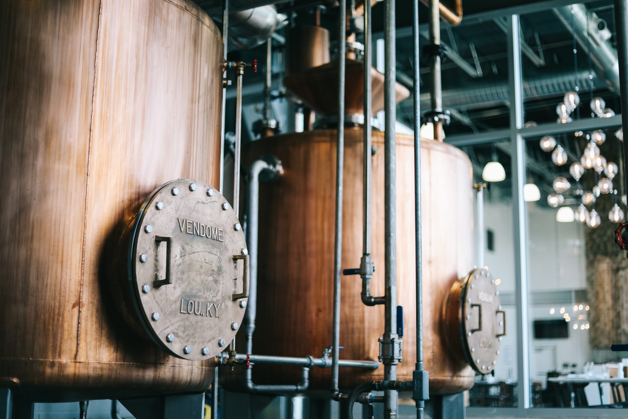 Copper still with a manway door inside a bright production hall