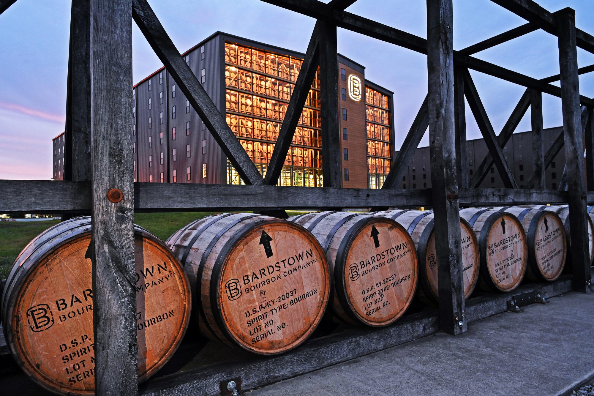 Barrels with Bardstown Bourbon Company branding on a rack in front of the warehouse