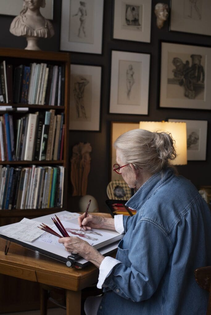 Claudia Hammer working at her drafting table in a studio lined with books and framed drawings