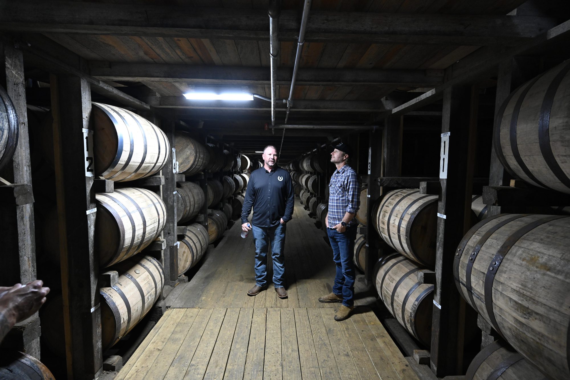 Two men standing in the aisle of a barrel rickhouse during a distillery tour