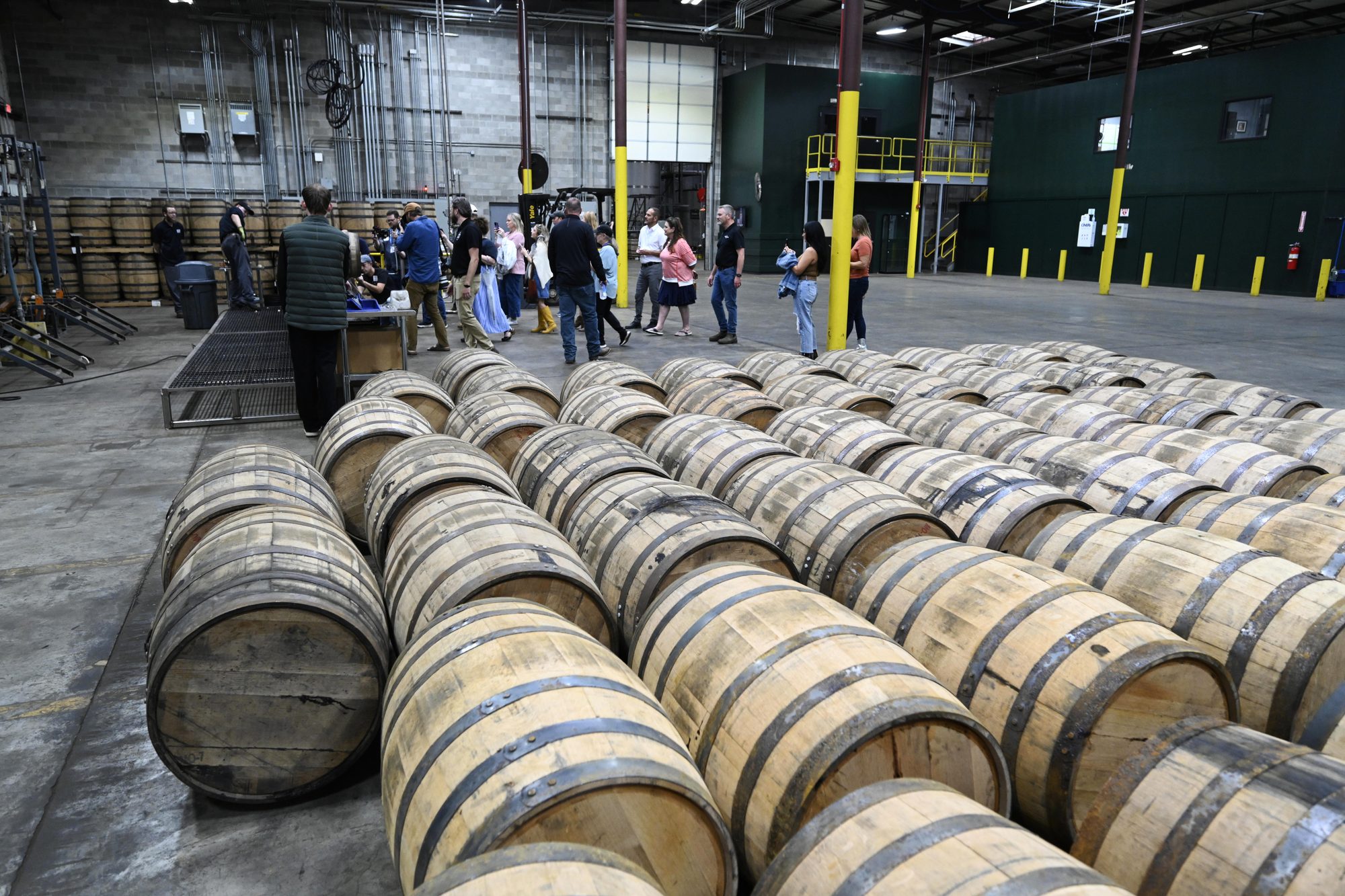 Rows of whiskey barrels in a warehouse with guests mingling in the background